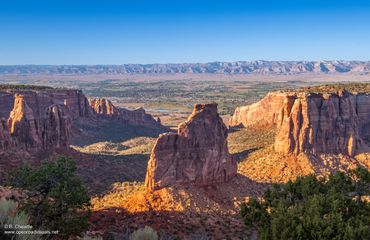 Sunlit rocky cliffs and canyon landscape under a clear blue sky.