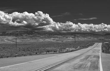 A long empty road stretches into the distance under dramatic clouds.