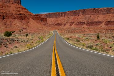 Open road leading through a red rock desert landscape under a clear blue sky.