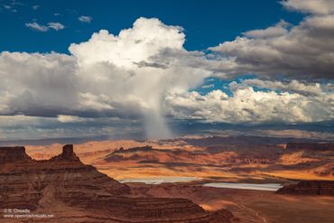 Clouds cast shadows over a rugged desert landscape with distant rain.