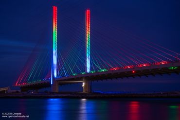 A cable-stayed bridge illuminated with colorful lights at night.