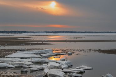 Winter sunset over a partially frozen lake with ice chunks and calm water.