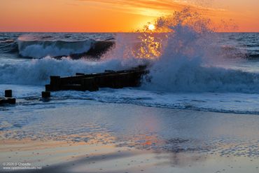 Sunset over ocean waves crashing against a jetty.