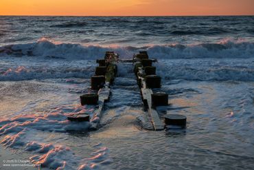 Old pier remnants stretch into the ocean at sunset.