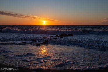 Sunset over ocean waves with scattered wooden planks in the water.