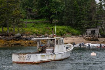 Old fishing boat named Geneva Sue docked near a forested shore.