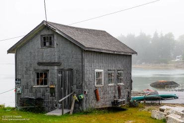 A small weathered boathouse by the water on a foggy day.
