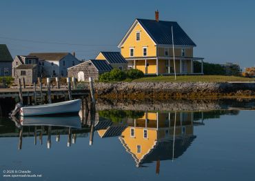 Yellow house reflected in calm water near docks.