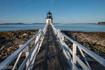A lighthouse connected by a wooden walkway on a rocky coast.