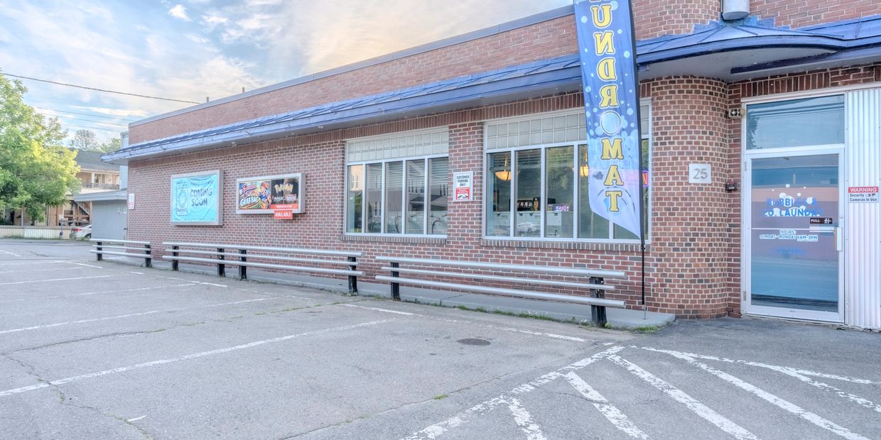 Exterior view of a laundromat with parking spaces and advertisements on the wall.