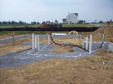 Construction site with foundation and pipes in progress near a house.