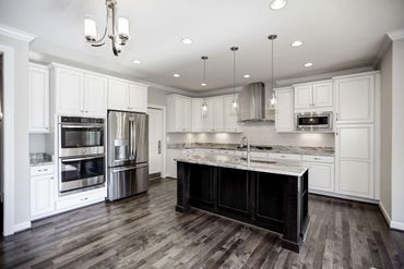 Modern kitchen with white cabinets and a black island on dark hardwood floors.