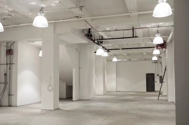 Spacious empty industrial warehouse with white walls and ceiling lights.