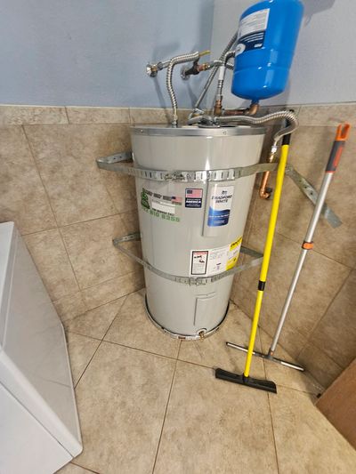A water heater installed in a tiled corner with cleaning tools nearby.