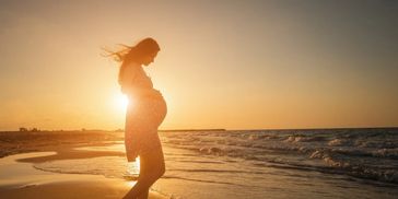 Pregnant woman standing on the beach at sunset.