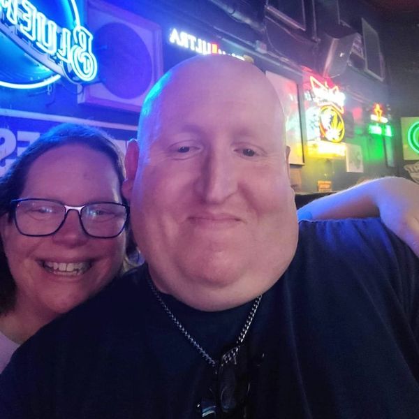 Two friends smiling in a neon-lit bar with colorful signs in the background.