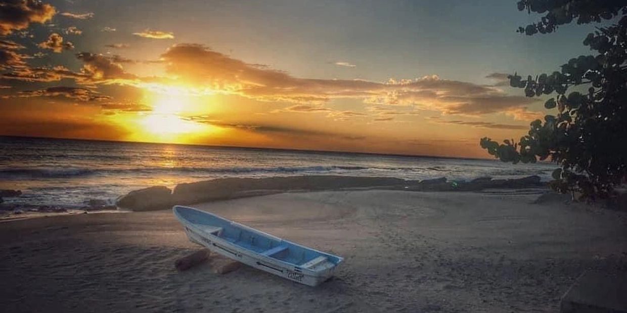 A boat rests on a beach at sunset with vibrant skies.