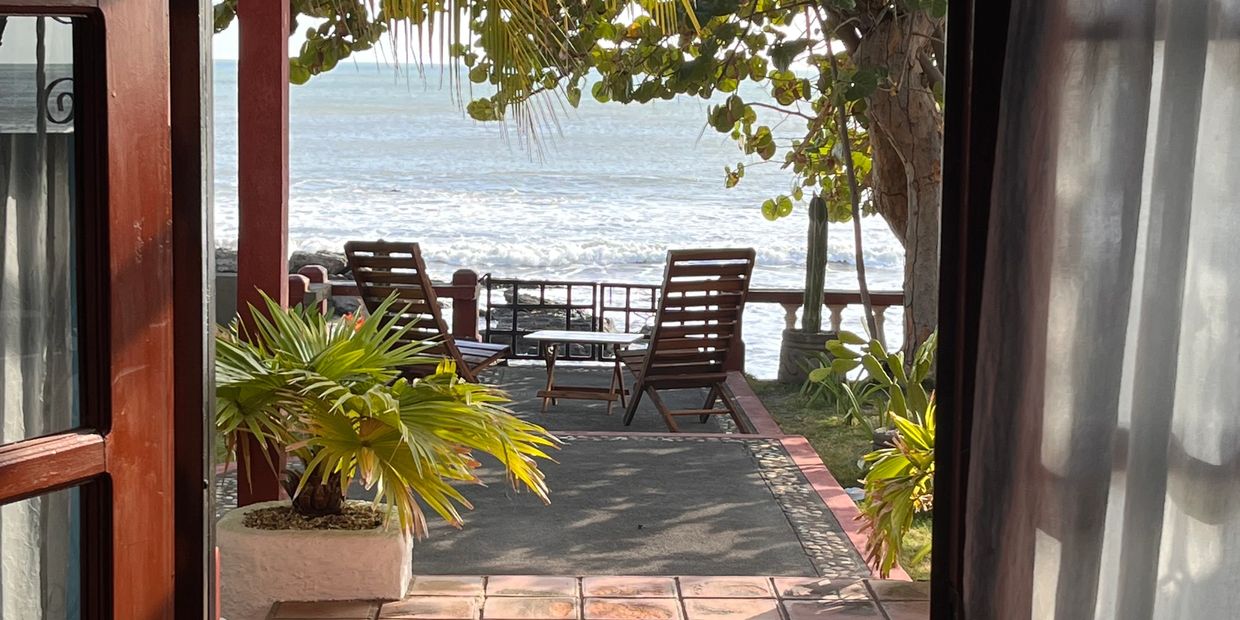 View of ocean from a cozy patio with chairs and plants.