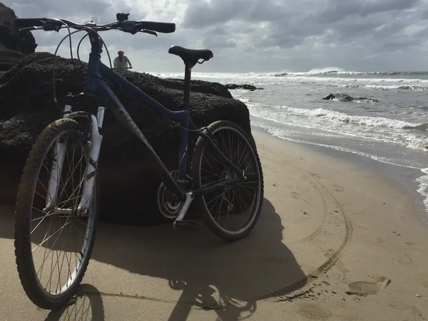 A bicycle parked on a sandy beach near the ocean with cloudy skies.