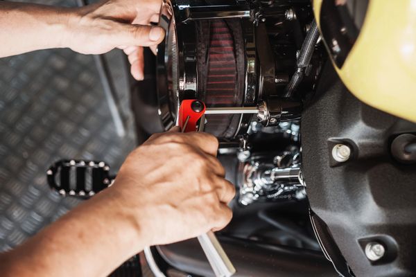 A close-up of a person's hands using a wrench to work on a motorcycle engine.