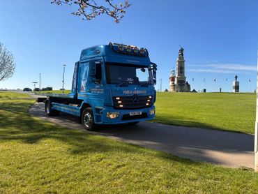 Blue flatbed truck parked near a monument on a sunny day.
