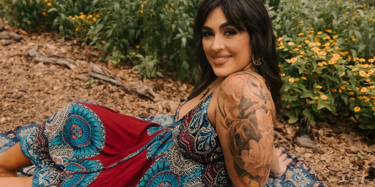 Dark haired woman sitting in rug on ground in garden smiling 