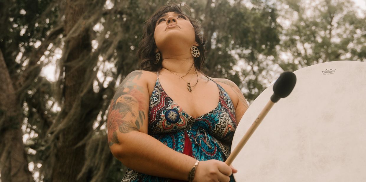 Dark haired woman holding large drum wearing burgundy dress 
