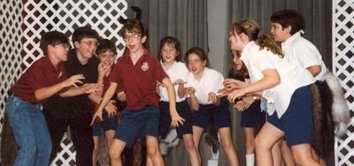 A group of children in school uniforms acting playfully on stage.