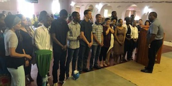 A group of people standing in a line listening to a speaker indoors.