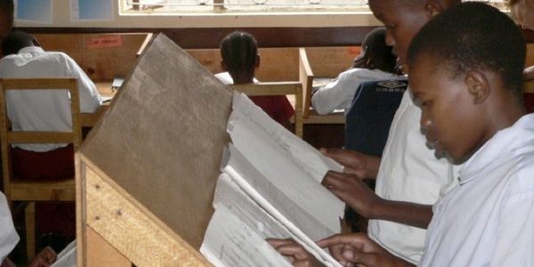 Students reading books in a classroom with wooden desks and chairs.