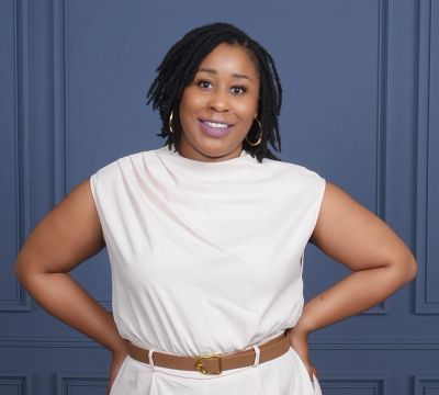 Confident woman in a white sleeveless top smiling against a blue paneled wall.