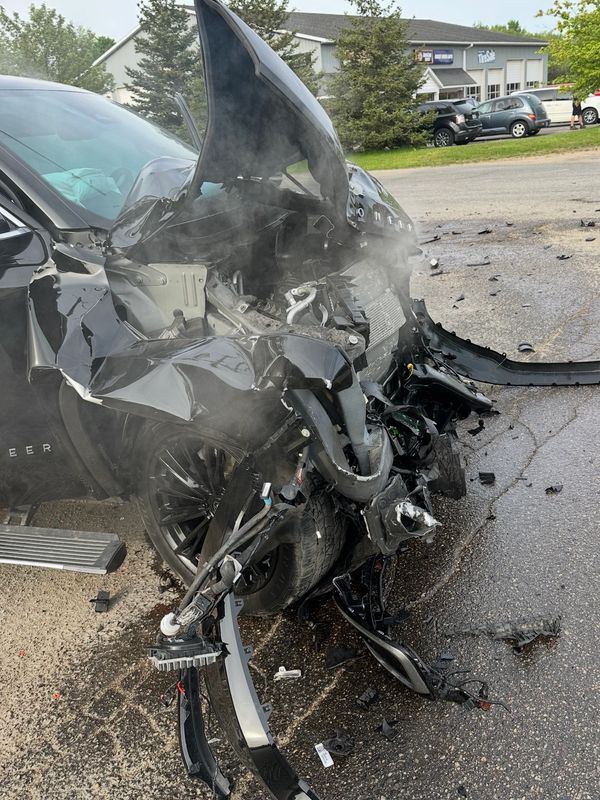 Severely damaged black SUV with front-end crushed and smoke rising after a collision.