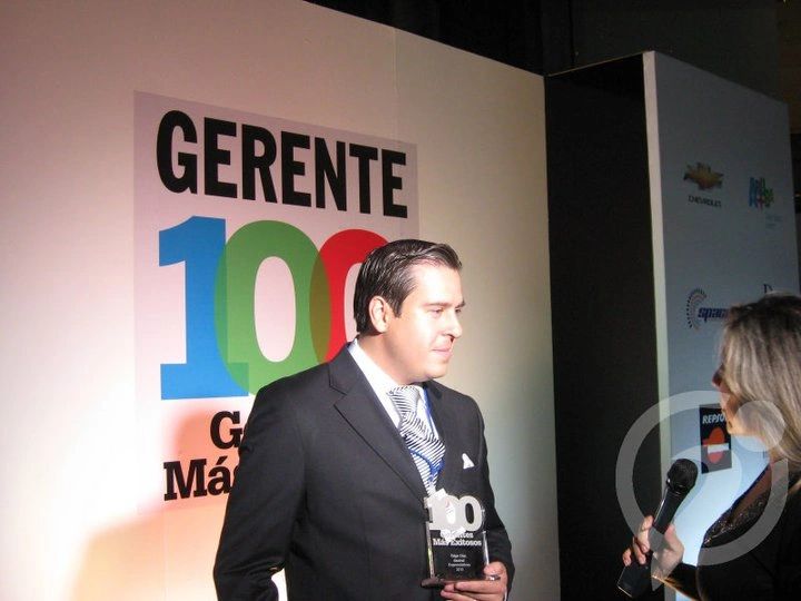 Man receiving an award at a corporate event with a 'GERENTE 100' sign.