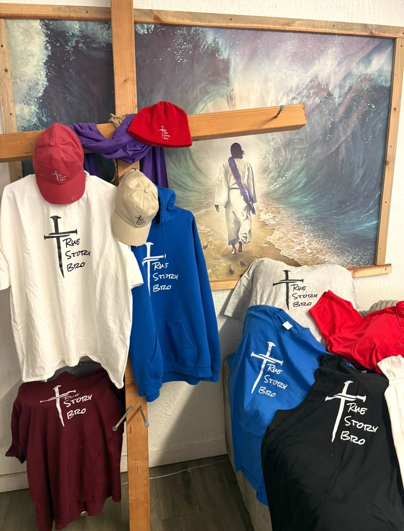 Christian-themed apparel displayed on a wooden cross against a backdrop of Jesus parting the sea.