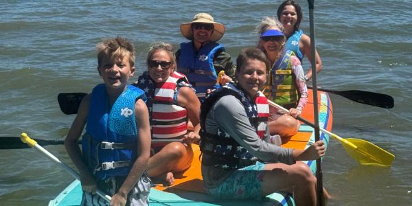 Group of six people kayaking on a lake, wearing life jackets.