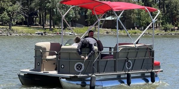 Man and child on a pontoon boat with a red canopy.