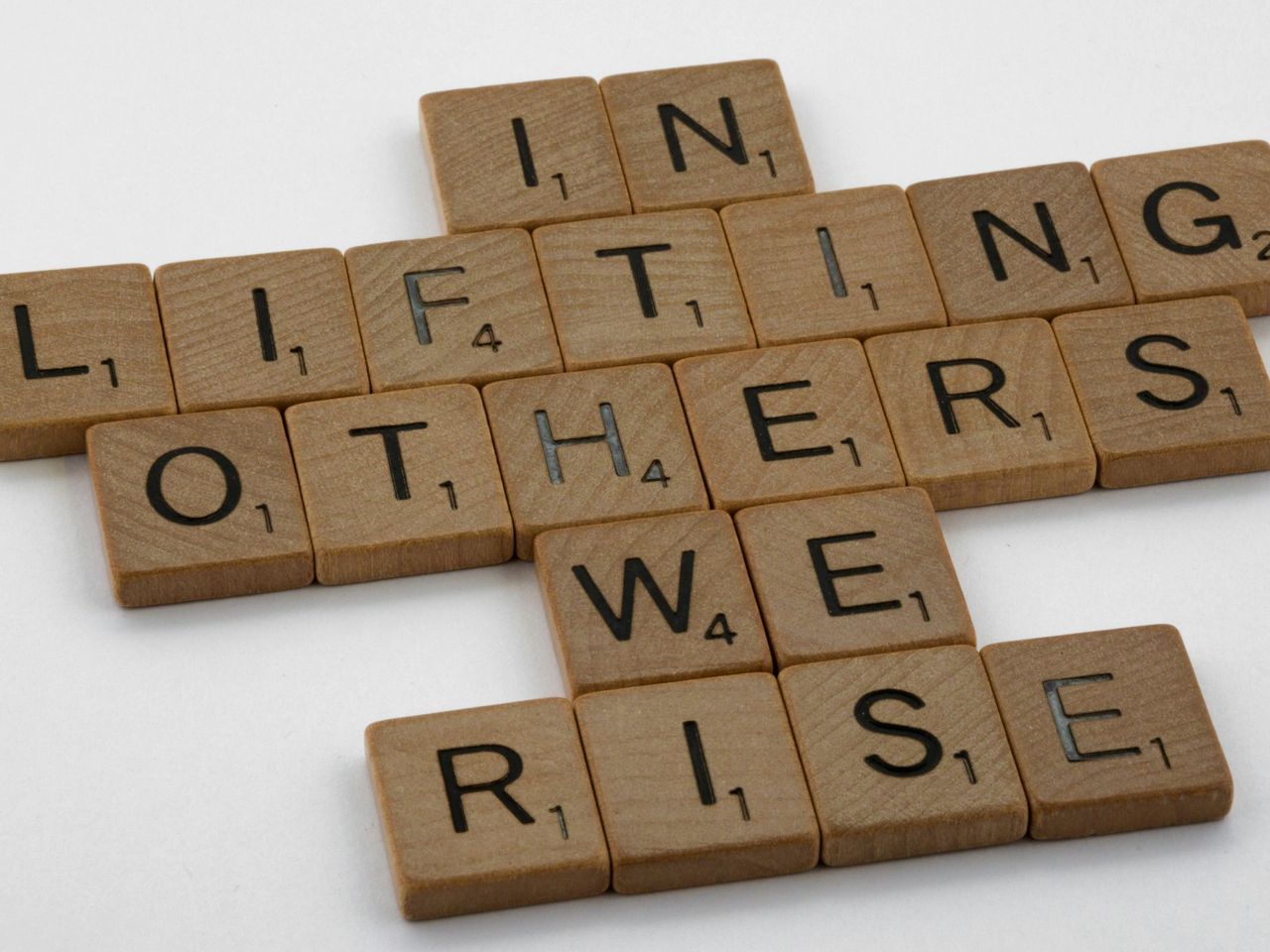 Scrabble blocks, spelling out the phrase, "In lifting others, we rise." Scrabble blocks, spelling out the phrase, "In lifting others, we rise."