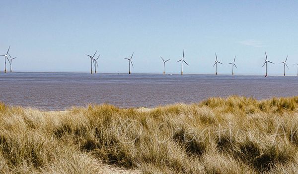 Caister on sea wind turbines out at sea, blue north sea with sandunes and sand in the forefront of i