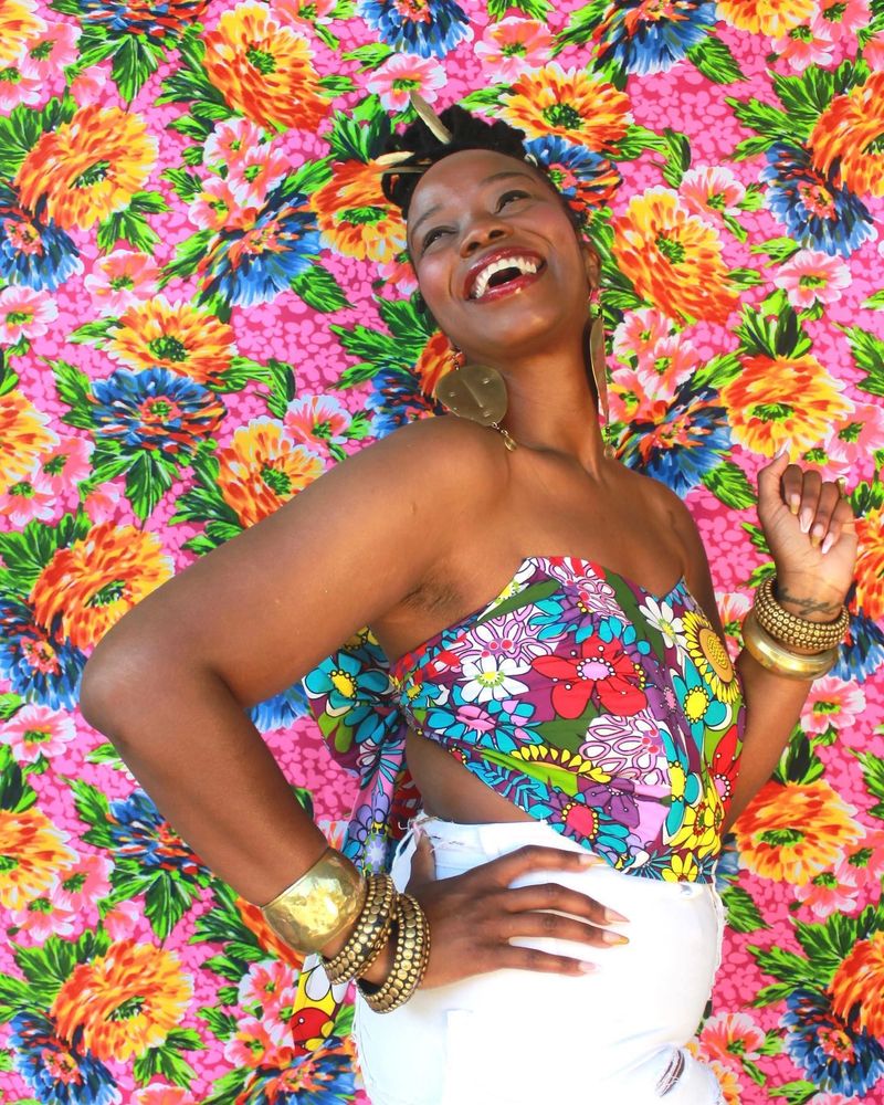 Brown-skinned woman smiling in a floral bustier in front of a floral backdrop.