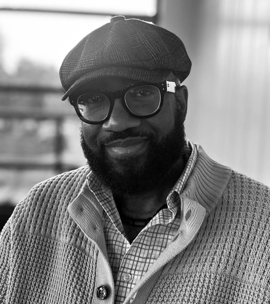 Launch the Author Founder Corwin Melvin wearing a cap, glasses, and a knitted sweater, smiling.