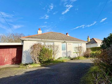 Single-story house with shrubs and a driveway under a blue sky.