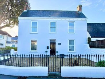 A white two-story house with a black door and fenced front yard.