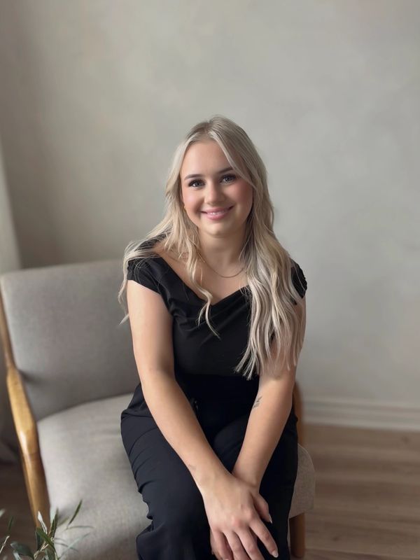 Young woman with long blonde hair sitting on a chair, smiling.