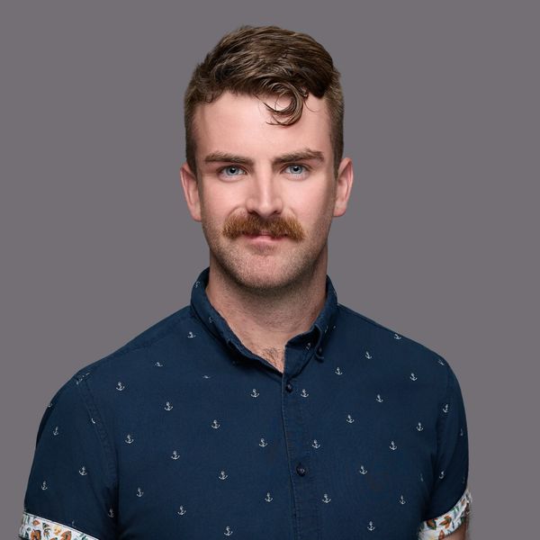 Man with a mustache and blue eyes wearing a navy anchor-patterned shirt.