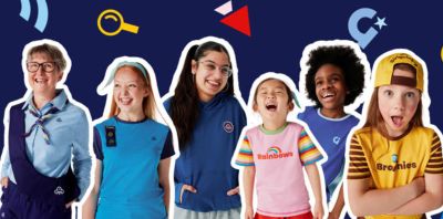 Group of six smiling kids and an adult in colorful outfits against blue background.