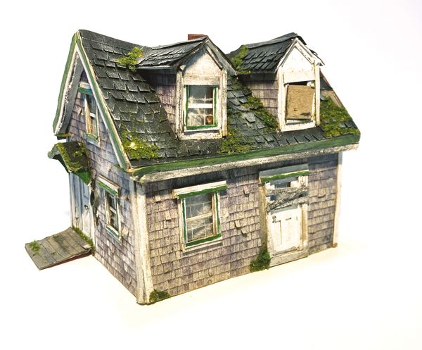 A small, detailed model of an old, weathered house with moss on the roof.