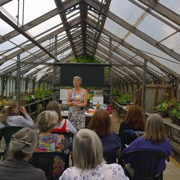 Teri Sayers-Cooper delivering a workshop in greenhouse with people seated and trainer standing 