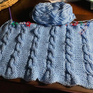 Blue knitted fabric with cable patterns in progress.