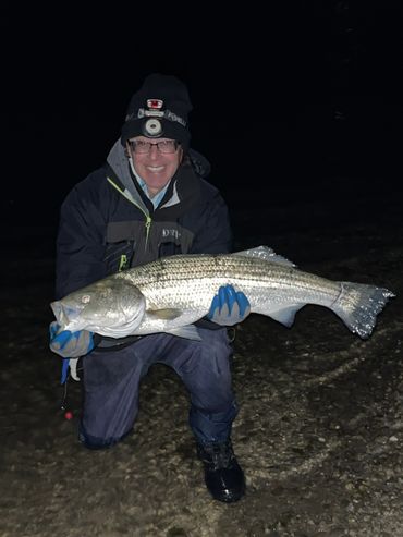 Person holding a large fish at night in outdoor gear.