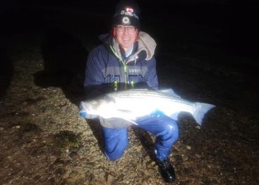 Person holding a large fish at night on a rocky shore.